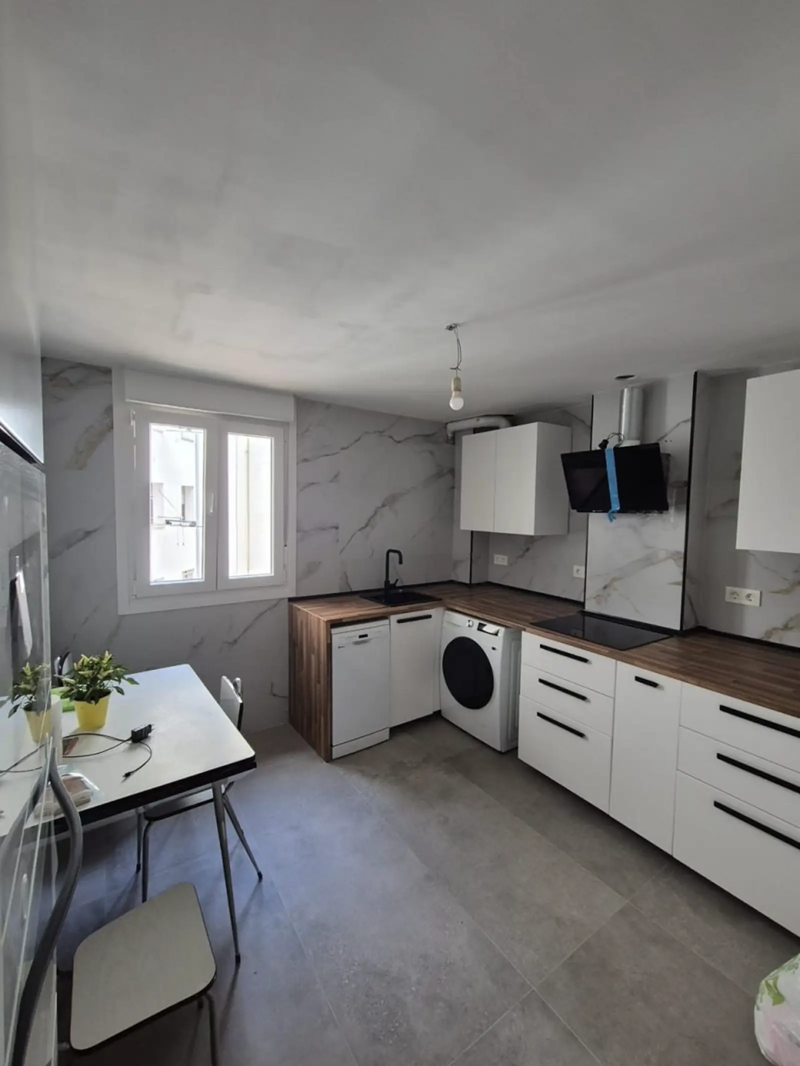 Cocina reformada con encimera efecto madera, electrodomésticos integrados y pared efecto mármol